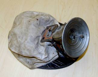 Photograph of cloth cap, with hard brim, and mining lamp attached.