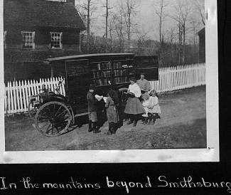 Book wagon with horse group of people standing in front of a house with white picket fence