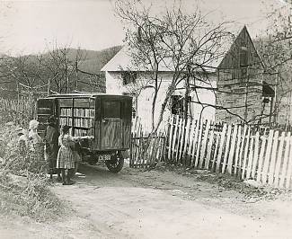 Book mobile stopped outside of house with picket fence and children looking through the books