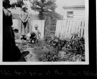 Bookwagon stops outside of home with white fence, mother and young child stand for photo