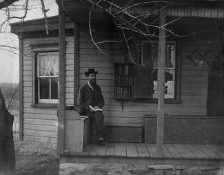 Man sitting on porch with book in hand near book deposit