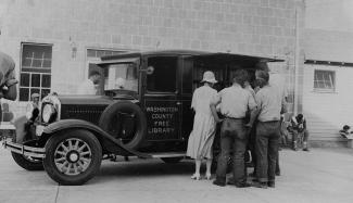 Bookwagon outside of penal farm; woman and 4 prisoners look through books