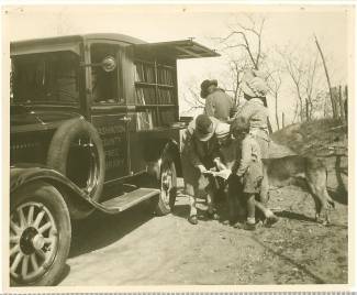 Book wagon on country road; women, children and a dog