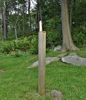 Broken post sign with directional sign missing; trees, grass and rocks in background