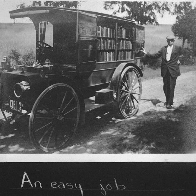 Motorized book wagon on a country road; man stand outside wagon