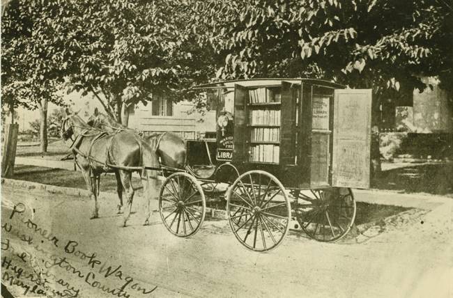 Book wagon with horses parked in front of a house