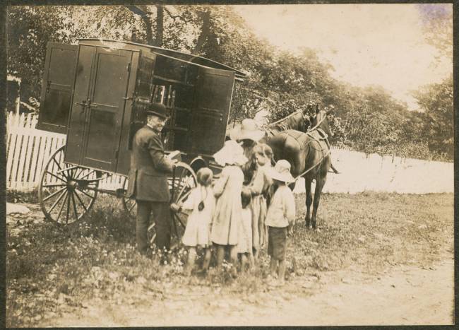 Image of bookwagon with 2 horses, man with several children handing out books