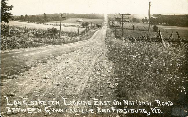 Black & white photo of country road circa 1900s; text states "looking East on National Road". 