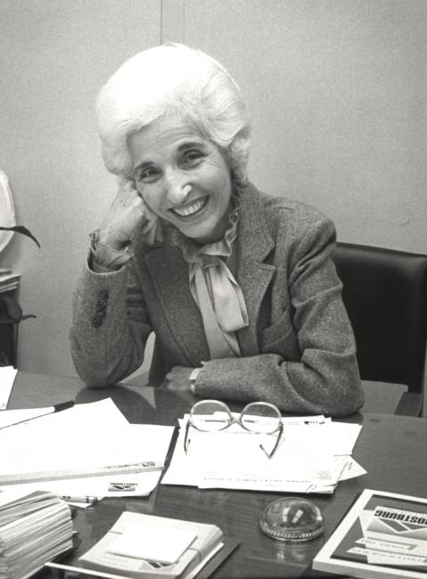B&W photo of Alice Manicur seated at desk with papers on desk and eye glasses