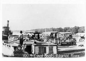 Multiple Canal boats docked by river; Text "100.9 Canal Boats Potomac River"