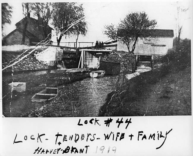 House with stream near, boat in stream.  Text written on photo "Lock #44, Lock-Tenders-Wife + Family Harvey Brant 1914"