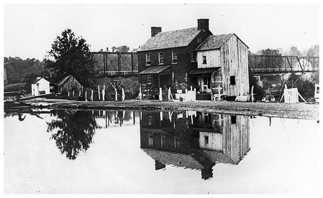 Lockhouse between the towpath and the river; railroad bridge runs behind house