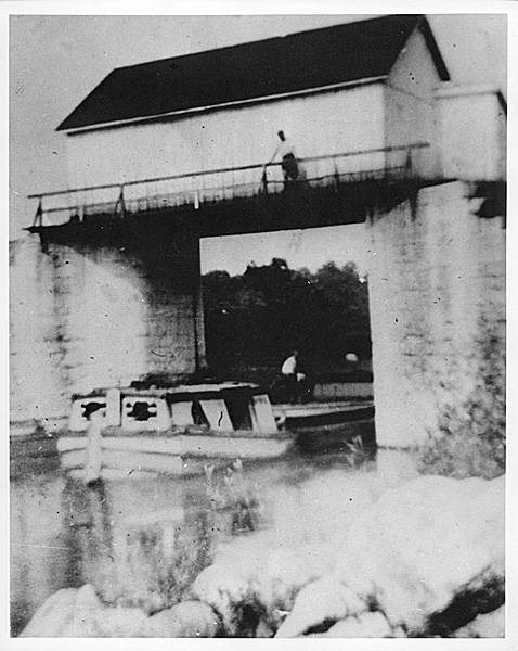 Stop gate at Dam 4; boat in canal, stone covered bridge over canal with person standing on bridge
