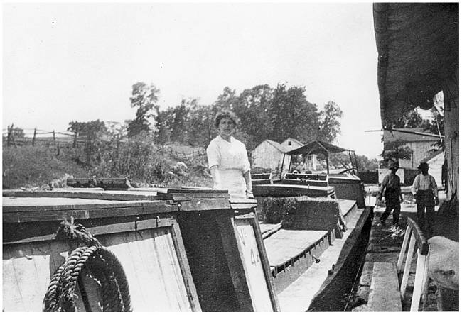 Woman stands on parked canal boat; 2 men walking on platform