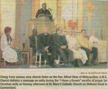 Group of 8; 1 speaking at podium, 7 seated in front in chairs at St. Mary's Catholic Church