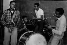 Photo of 4 band members playing drums and 3 saxophone players