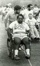 Photo of man in wheel chair race being pushed by a man; other racers in background
