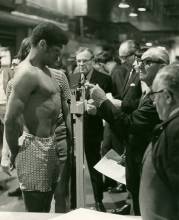 Boxer stands on scale to weigh in for competition; judges stand around in background