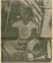 Man sitting on curb drinking from a bottle celebrating with crowd the end of WWII in Baltimore MD