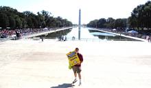 Image of man holding a sign in front of the National Monument water pool