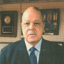 Cropped image of Randolph W. Bromery with plaques and photos on pegboard in background