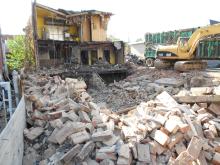 Bulldozers knock down building with brick rumble in foreground