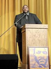 Man standing behind podium; picture of MLK in front of podium