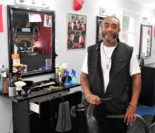 Barber Derik Stephens poses in front of his barbershop chair seat