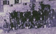 8 Stable hands sitting in front of horses + 1 stable hand standing