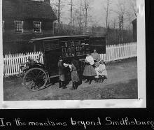 Book wagon with horse group of people standing in front of a house with white picket fence