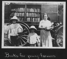 Two boys and a girl stand by the bookmobile holding their selections