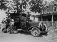 Book wagon parked in front of a home with stick fence; family of 6 looks through books