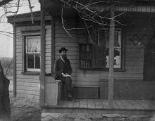 Man sitting on porch with book in hand near book deposit