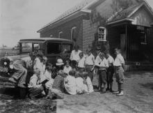 Book wagon in country by house; children listening to librarian read story