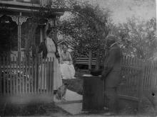 Two women outside behind fence, man with deposit box standing outside opened fence gate