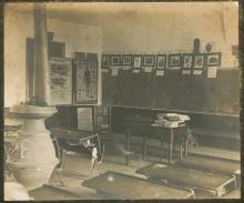School room with desks and blackboard; wood stove in middle of room