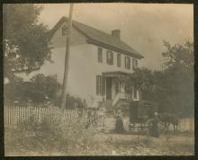 Book wagon with horse with people standing in front of a house with white picket fence