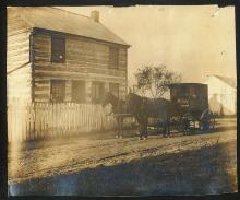 Book wagon with 2 horses standing in front of a log house with picket fence