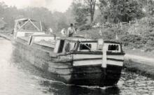 Canal boat in river with man steering boat at top 