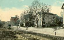 Colorized post card of street car trolley coming down road; houses on the right. 