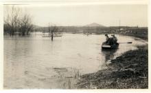 Photo of East End of Hancock, MD during 1936 Flood; 3 people in boat rowing past top of telephone pole