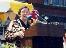Photo of Dr. Catherine R. Gira speaking at a podium with multiple microphones