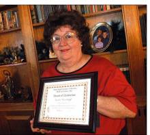 Photo of Sandra Grandstaff holding a framed certificate in personal library