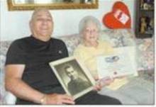 Photo of man and woman sitting on couch holding photos; Richard and Dorothy Mellotte