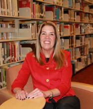 Photo of Cherie Krug sitting in chair at library with book stacks in background