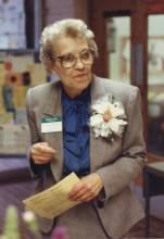 Photo of Edith G. Brock, with flower on lapel holding a paper