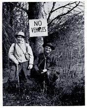 2 men on canal with sign on tree that says "No vehicles"