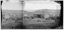Circa 1862 photo of barn used for hospital; white tents pitched in background, horses and soldiers outside 