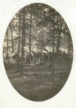 Circa 1862 photo of wooded area with white tents pitched, men carrying man on stretcher, men walking around