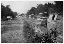 Multiple canal boats in line stuck in low water area along canal waiting for rain